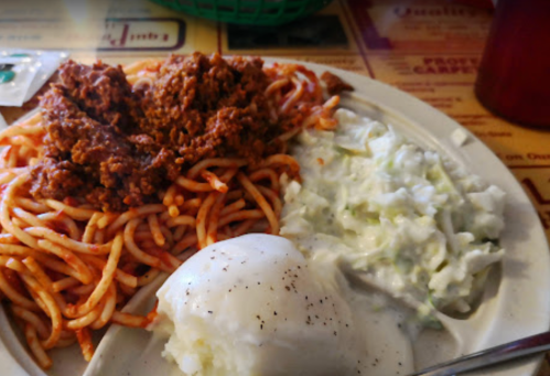 A plate of spaghetti topped with chili, a side of coleslaw, and a scoop of mashed potatoes.