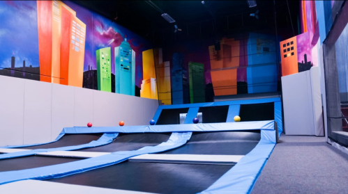 A colorful indoor trampoline park with multiple trampolines and vibrant cityscape murals on the walls.