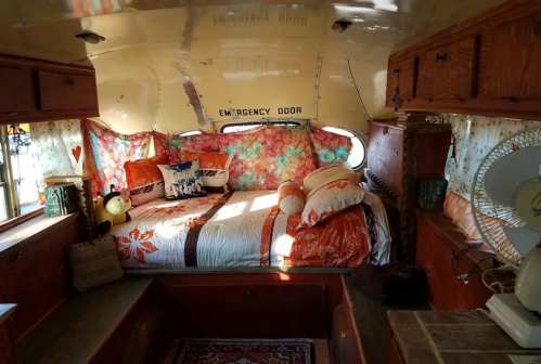 Cozy interior of a vintage camper, featuring a floral bedspread, decorative pillows, and warm wooden accents.