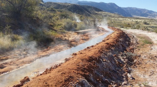 A steaming, narrow waterway flows through a dry, desert landscape with mountains in the background.