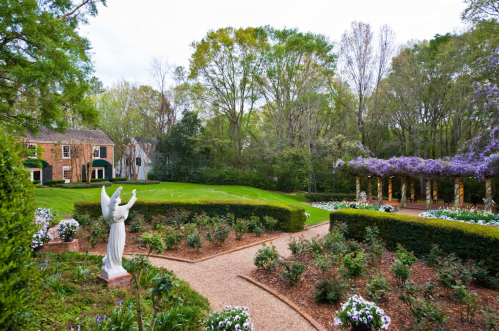 A serene garden with a statue of an angel, blooming flowers, and a charming house in the background.