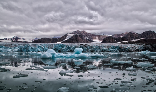 A serene glacial landscape with icebergs floating in calm waters, surrounded by rugged mountains under a cloudy sky.