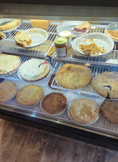 A display case filled with various baked pies, including fruit and cream varieties, on a wire rack.