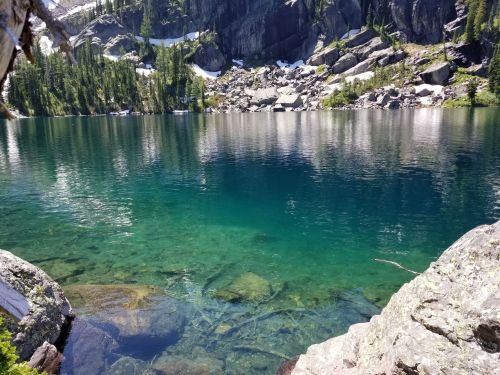 A serene lake surrounded by rocky cliffs and lush greenery, with clear turquoise water reflecting the landscape.