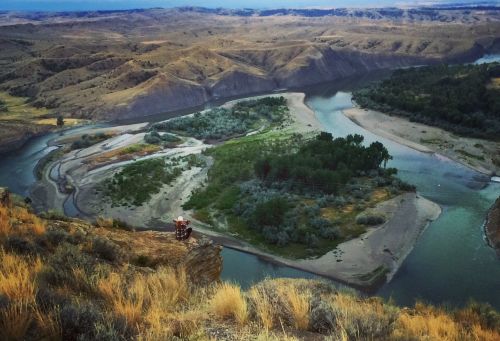 A scenic view of a winding river surrounded by green vegetation and rolling hills under a clear sky.