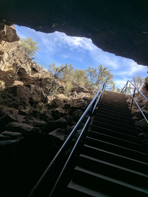 View from inside a cave looking up at a staircase leading to a bright sky and trees above.