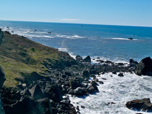 A rocky coastline with waves crashing against the shore under a clear blue sky.