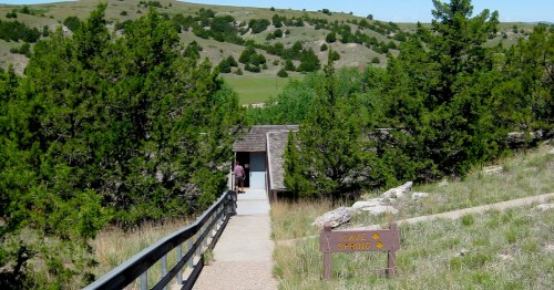 A pathway leads to a building surrounded by greenery and hills, with a sign pointing to a spring.