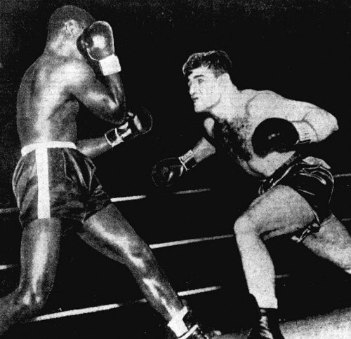 A black-and-white photo of two boxers in a ring, one throwing a punch while the other defends.