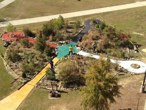 Aerial view of a colorful garden with winding paths and people working among plants and rocks.
