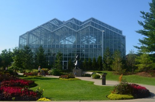 A large glass greenhouse surrounded by colorful flowers and greenery on a sunny day.