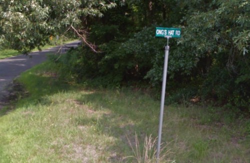 A street sign for Ong's Hat Rd, surrounded by greenery and a road in the background.