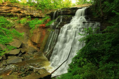 A serene waterfall cascading over rocky cliffs, surrounded by lush green foliage and a tranquil stream below.