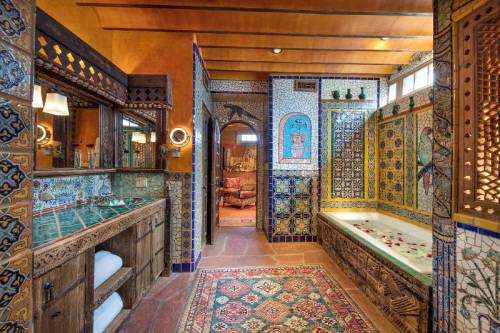 A beautifully tiled bathroom featuring intricate patterns, a soaking tub, and a wooden vanity with towels.