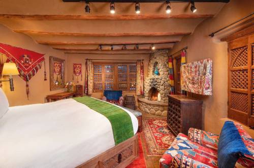 Cozy bedroom with rustic decor, a stone fireplace, colorful textiles, and wooden beams, creating a warm atmosphere.