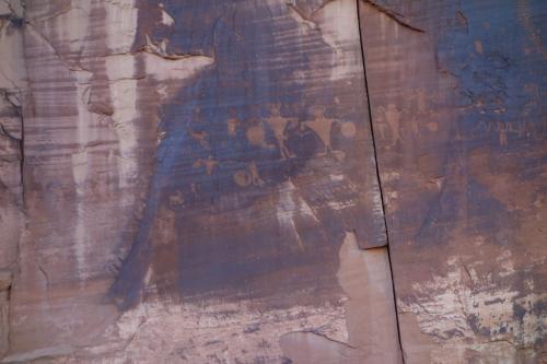 Petroglyphs etched into a rocky surface, depicting abstract human figures and symbols in earthy tones.