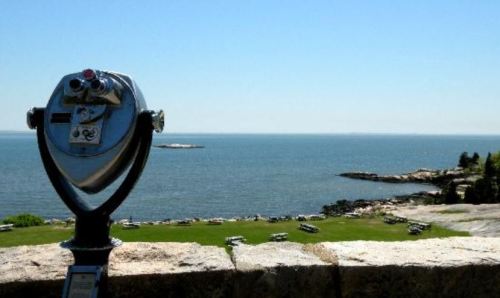 A coin-operated telescope overlooks a calm sea and distant island under a clear blue sky.