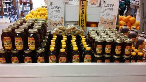 Display of jars of local honey with a sign that reads "Love and bee Loved," surrounded by fresh fruits.