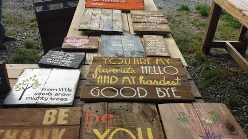 A collection of wooden signs with various inspirational quotes and messages displayed on a table outdoors.