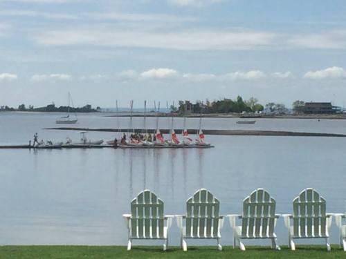 A serene lake view with sailboats in the distance and white Adirondack chairs in the foreground.