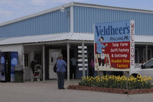 A blue building with a sign for Veldheer's Tulip Farm and Wooden Shoe Factory, featuring colorful tulips in front.