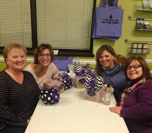 Four women smile around a table decorated with gift baskets and products, in a cozy, well-lit room.