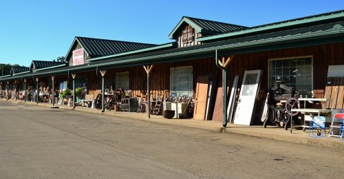A rustic storefront with wooden siding, displaying various antiques and items outside under a clear blue sky.