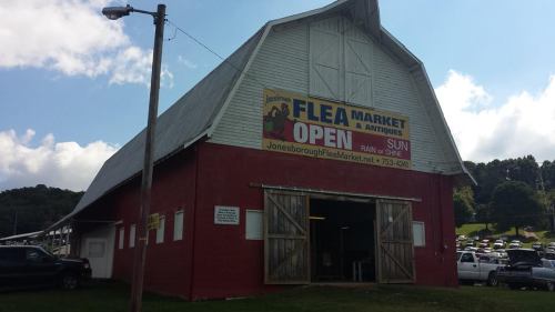A red barn-style building with a sign for a flea market, featuring "OPEN" and "SUNDAYS" in large letters.