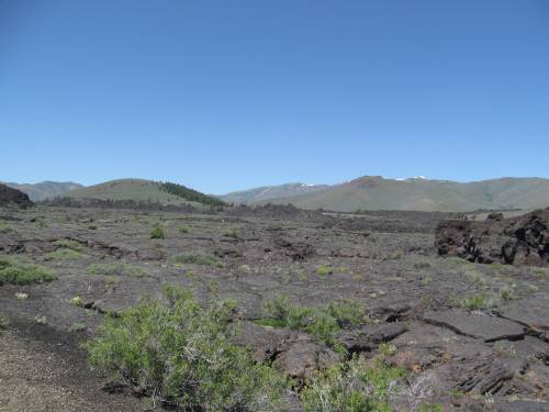A vast, rocky landscape with sparse vegetation and distant mountains under a clear blue sky.