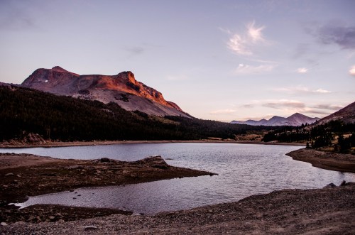 A serene lake surrounded by mountains at sunset, with soft clouds in the sky and a tranquil landscape.