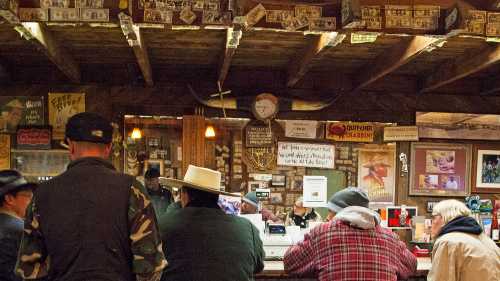 A rustic bar scene with patrons sitting at the counter, surrounded by vintage decor and memorabilia on the walls.