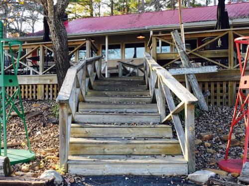 Wooden stairs lead up to a rustic building surrounded by trees, with colorful structures on either side.