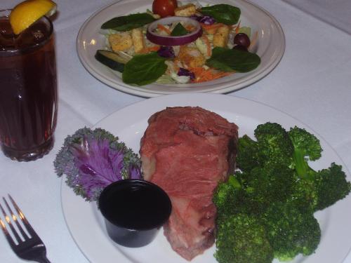 A plate with sliced roast beef, steamed broccoli, and a dipping sauce, alongside a salad and iced tea.