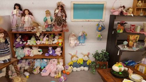 A cozy thrift store display featuring dolls, stuffed animals, and various decorative items on shelves and tables.