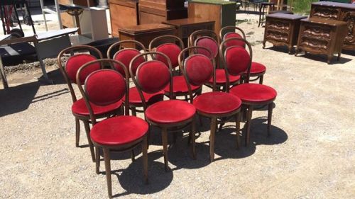 A group of vintage wooden chairs with red velvet seats arranged in a sunny outdoor setting.