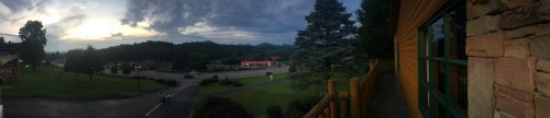 Panoramic view of a scenic landscape at dusk, featuring mountains, trees, and a parking area.