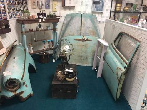 Vintage decor featuring rusted car parts, a lamp, and various collectibles in a cozy shop setting.