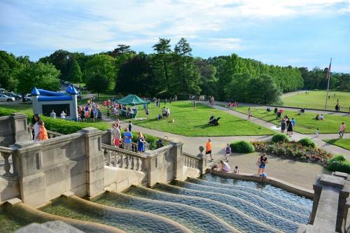 A park scene with people enjoying the outdoors, featuring steps leading to a water feature and green trees in the background.