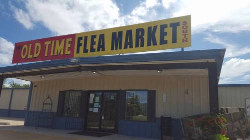 Sign for "Old Time Flea Market" on a building with a blue sky and clouds in the background.