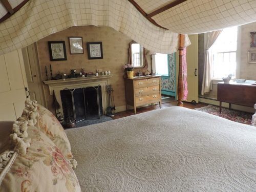 Cozy bedroom with a canopy bed, vintage furniture, and a decorative fireplace, featuring warm, inviting decor.
