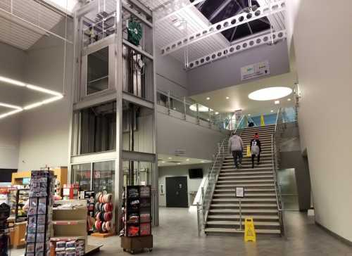 Interior view of a modern building featuring a staircase, elevator, and a retail area with various items for sale.