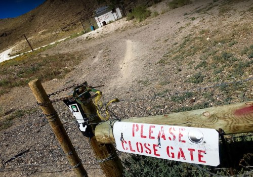 A weathered sign on a gate reads "PLEASE CLOSE GATE," with a dirt path and mountains in the background.