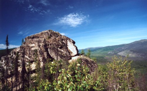 A rocky outcrop surrounded by lush greenery and rolling hills under a clear blue sky.