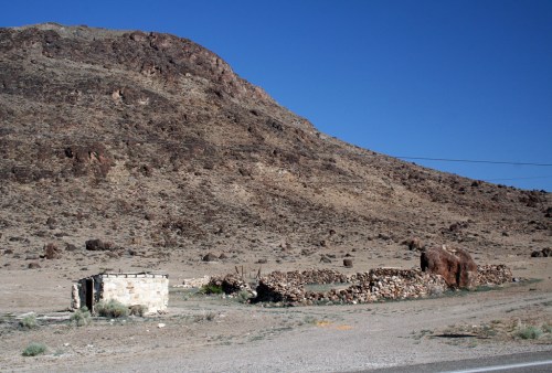 Abandoned stone structures in a barren landscape with a mountain in the background under a clear blue sky.