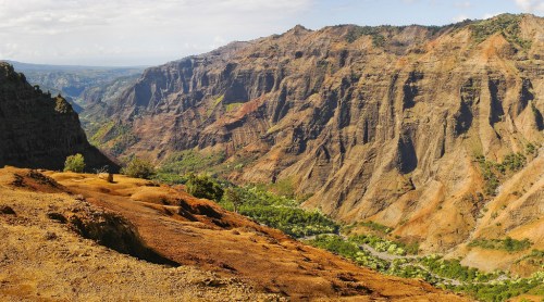 A panoramic view of a rugged canyon with colorful rock formations and lush greenery in the valley below.