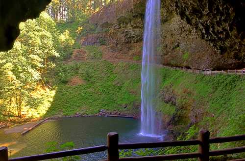 A serene waterfall cascades into a tranquil pool, surrounded by lush greenery and rocky cliffs.