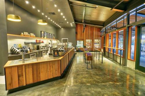 Modern coffee shop interior with a wooden counter, seating area, and large windows, featuring a sleek, minimalist design.