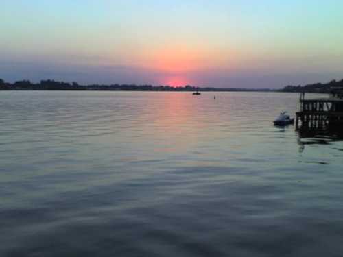 A serene sunset over a calm lake, with soft pink and purple hues reflecting on the water's surface.