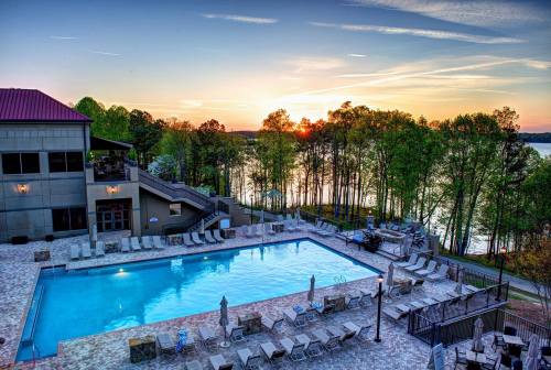 A serene poolside view at sunset, surrounded by trees and a calm lake, with lounge chairs arranged around the pool.