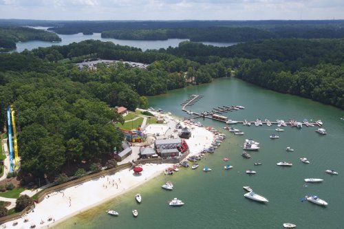 Aerial view of a beach area with boats, a water park, and lush green surroundings by a lake.